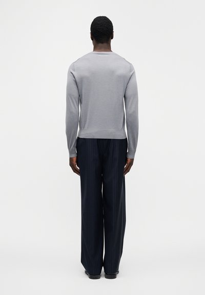 Pull en tricot gris à col rond, associé à un pantalon large à rayures fines bleu marine. Texture lisse, ajusté à la taille, manches longues.