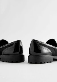 Mustad musta nahast kingad lakknaha aksentidega, brogue-detailidega ja tekstuuriga sametist külgedega. Paksud mustad tallad, millel on haardepind.