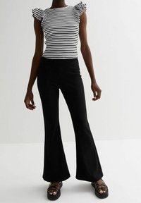 Pantalones negros acampanados combinados con una blusa de rayas en blanco y negro de canalé con mangas cortas con volantes. Tejido suave, diseño causal.