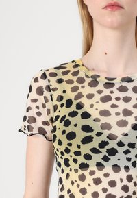 Top trasparente a maniche corte con stampa leopardata in giallo e nero, orlo a scallop e scollatura rotonda. Tessuto leggero.