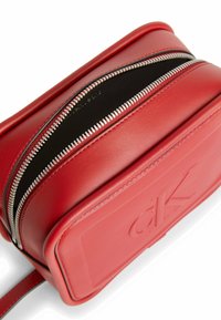 Bolso de cuero rojo con cierres de doble cremallera, textura suave, forma rectangular y logo en relieve en la parte frontal.