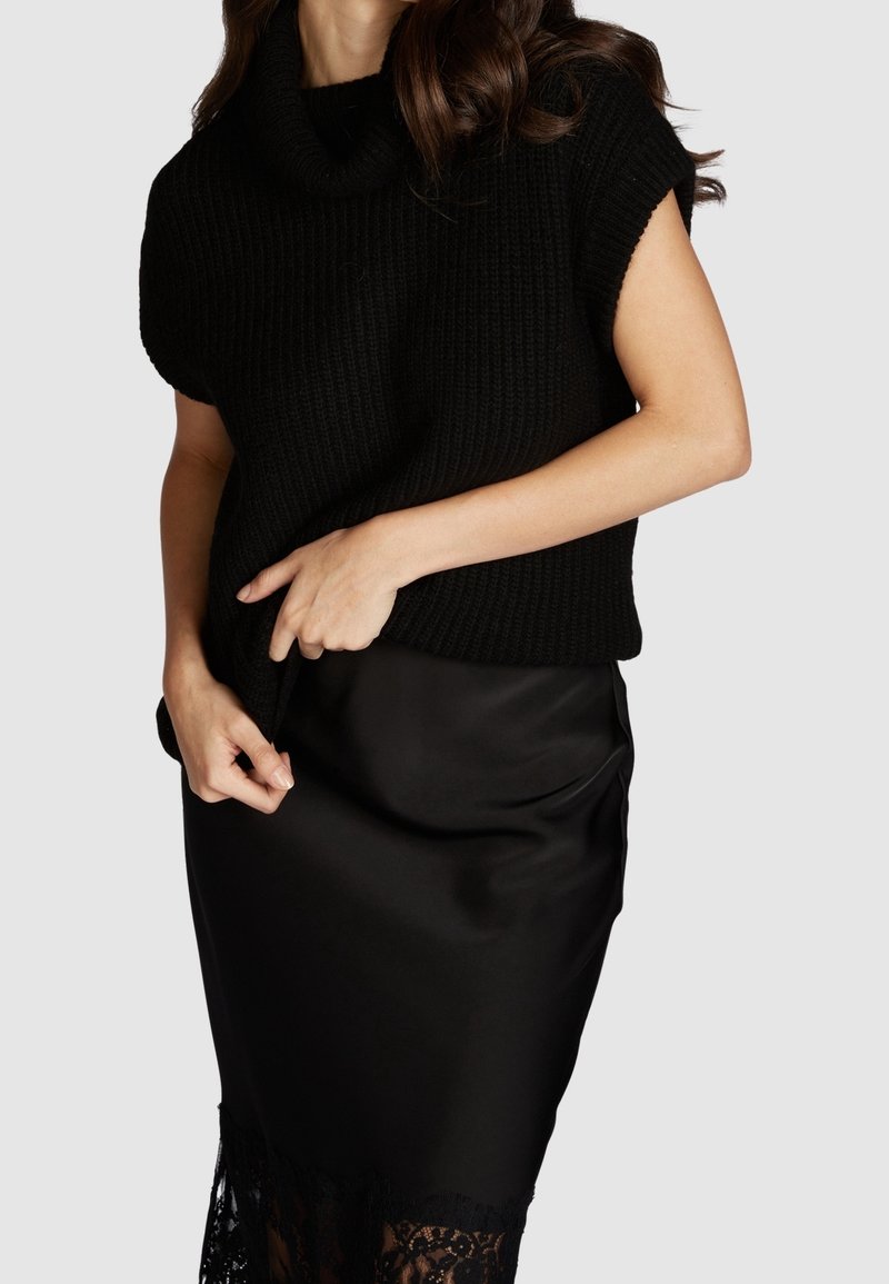 Pull en maille noire à col bénitier, associé à une jupe en satin noir avec une bordure en dentelle le long de l'ourlet. Matières texturées et lisses.