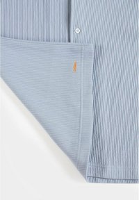 Vaaleansininen, ribbikankainen paita, jossa on nappikiinnitys. Helman lähellä on pieni oranssi logo. Silkkinen rakenne, rento muotoilu.