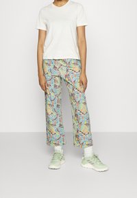 Printed wide-leg pants in light blue, featuring a colorful abstract pattern. Paired with a plain white t-shirt and light green athletic shoes.