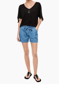 Svart kortärmad topp, v-ringad halsringning, upplagda ärmar; blå shorts med dragsko; svarta flip-flops med texturerad detaljering; enkla lager på lager-halsband.