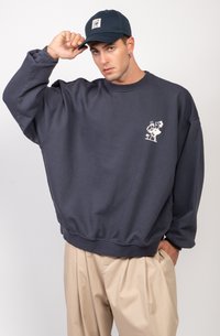 Sudadera de gran tamaño en color navy con puños y dobladillo acanalados, que presenta un estampado gráfico blanco en el pecho; combinada con pantalones beige de pliegues.