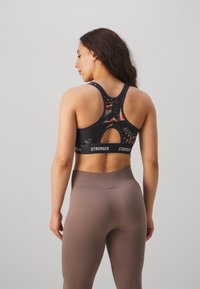 Top sportivo nero con un motivo astratto colorato, design a schiena scoperta e apertura a chiave. Abbinato a leggings beige a coste a vita alta.