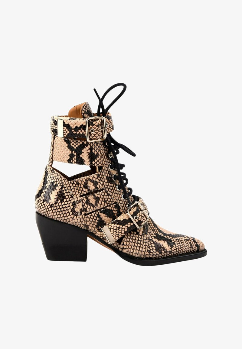 Bottine à talon hauteur cheville avec imprimé serpent beige et noir, côtés découpés, lacets noirs et deux boucles argentées sur un talon bloc noir.