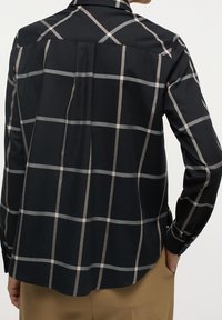 Chemise à carreaux noire avec fines rayures beige et grises. Manches longues, col classique et coupe décontractée avec un ourlet arrondi.