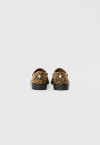 Brown leopard print shoes with a flat black sole. The design features a smooth texture and a round emblem on the heel.