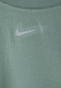Zaļš Nike sporta krekls ar baltu Nike swoosh logotipu uz krūšu daļas un redzamām šuvēm ap apaļo dekoltē.