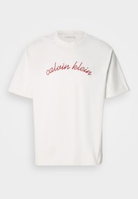White cotton t-shirt with short sleeves featuring curved red embroidered text "calvin klein" across the chest. Classic crew neck design.
