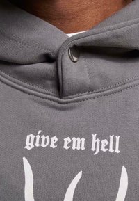 Grå hettegenser med ribbet tekstur, med et fremtredende hvitt trykk som sier "give em hell" over stiliserte hvite horn.