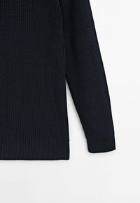 Manche de pull tricoté bleu marine avec détails sur le côté, poignets et ourlet côtelés sur fond blanc.