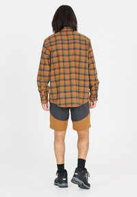 Oranssi ja vihreä ruudullinen pitkähihaisen paita, yhdistettynä vaaleanruskeisiin ja harmaisiin kahteen sävyyn lyhyisiin housuihin, sekä mustiin vaelluskengiin. Yksinkertainen nappikiinnitys.