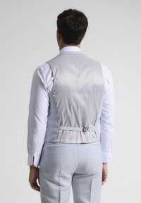 Chaleco de satén gris con una textura suave y hebilla ajustable en la parte posterior. Combinado con una camisa blanca, visto desde atrás.