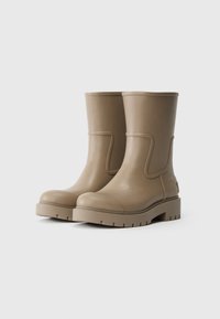 Stivali alla caviglia in gomma beige con punta tonda, tacco basso e pannello laterale decorativo. Presentano una suola testurizzata per una buona aderenza. Finitura liscia.