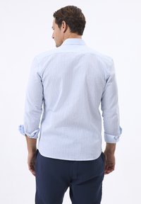 Camisa de botones a rayas azul claro con un corte ajustado en la parte trasera, mangas enrolladas y un cuello clásico, hecha de una tela suave.