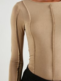 Langärmliges Oberteil aus leicht beigem Rippstoff mit Nahtdetails an den Ärmeln und dem Oberkörper sowie einem runden Halsausschnitt.