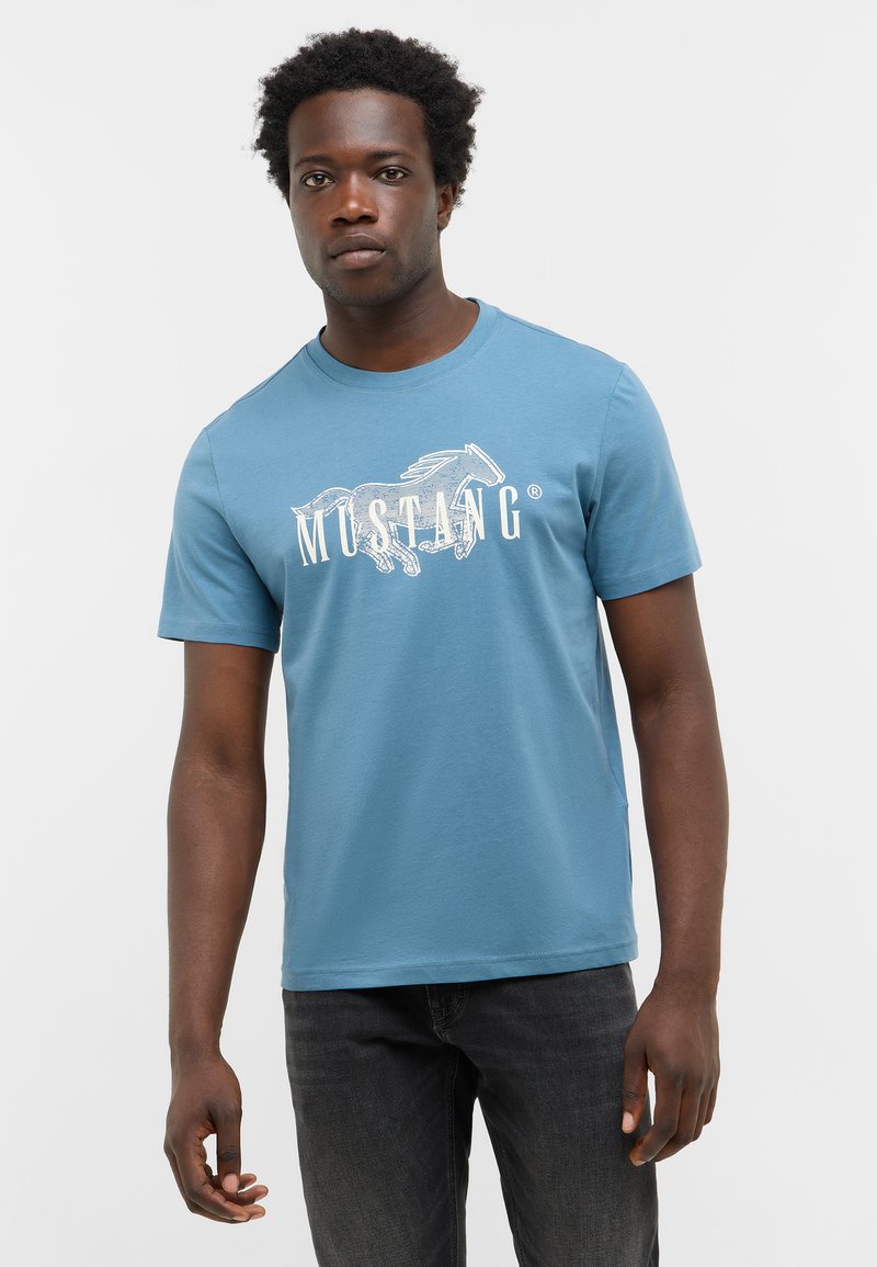 T-shirt en coton bleu à manches courtes, col rond, avec un logo blanc "MUSTANG" et un graphique de cheval sur la poitrine.