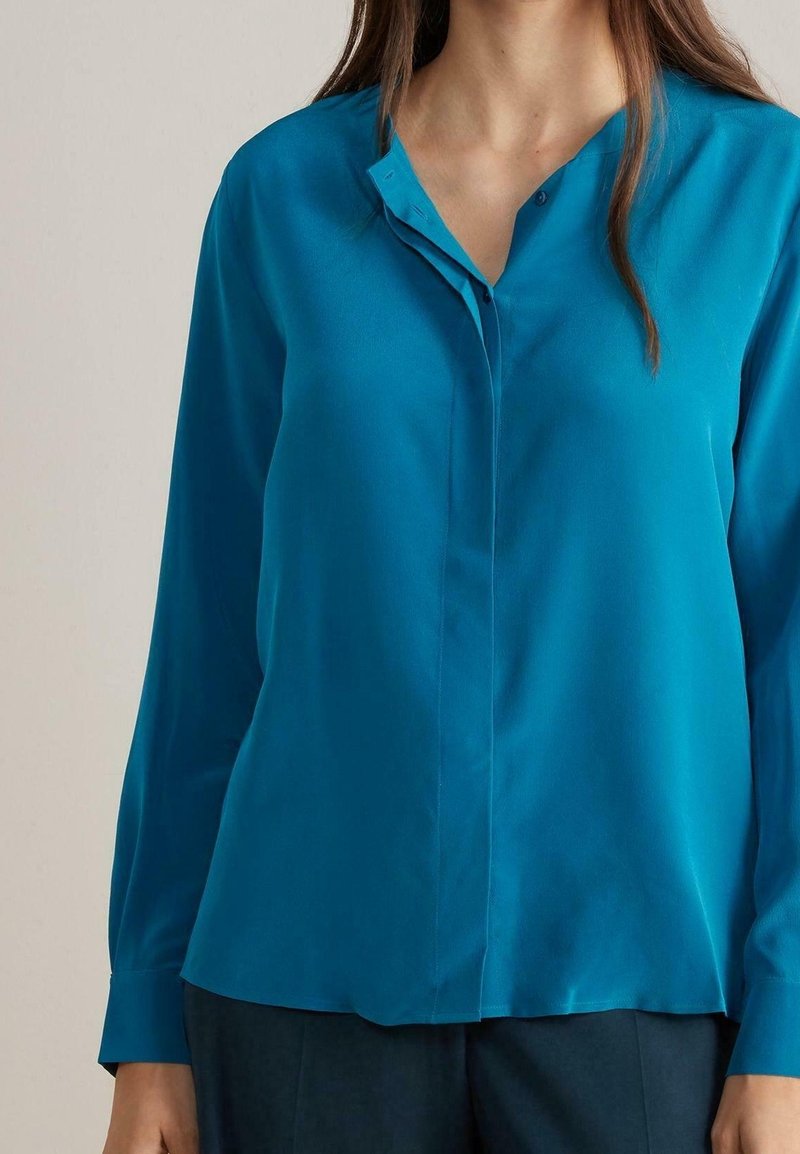 Turquoise button-up blouse, lightweight fabric, long sleeves, V-neck collar, with a smooth texture and a tailored fit. No visible patterns.