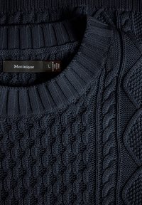 Mornarsko modra pletena pulover s teksturiranimi vzorci, vključno z vrvasto zasnovo in rebrastim ovratnikom. Nalepka navaja "Matinique", velikost L.