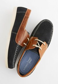 Scarpe casual da uomo nere e marroni realizzate in suede e pelle; presentano cuciture bianche, suola in gomma e accenti beige.