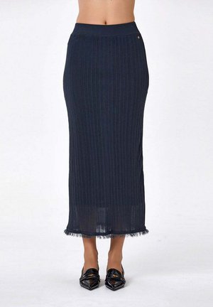 Jupe midi côtelée bleu marine taille haute avec ourlet effiloché, associée à des mocassins noirs à bout pointu, portée par une personne debout.