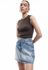 Braunes geripptes Tanktop, kombiniert mit einem verblassten blauen Jeans-Minirock. Der Rock hat ein Fünf-Taschen-Design und eine Knopfverschluss aus Metall.