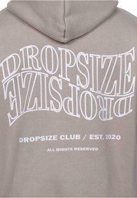 Grå hættetrøje med stort hvidt tekst, der står "DROPSIZE" i et buet design, med "DROPSIZE CLUB / EST. 2020" nedenfor i mindre skrifttype.