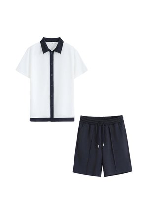 Chemise blanche à manches courtes avec boutons, col noir et bordure, associée à un short noir à cordon.