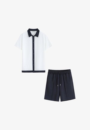 Chemise blanche à manches courtes avec boutons, col noir et bordure, associée à un short noir à cordon.