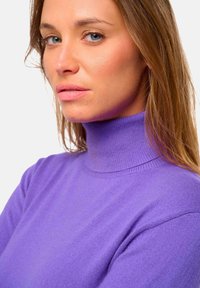 Pull turtleneck violet en matériau tricoté, avec un design ajusté et un col côtelé. Gros plan sur l'encolure et les épaules.
