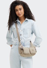 Beige Schultertasche aus weichem Stoff, mit zwei Vordertaschen, einem dezenten gesteppten Muster und einem dekorativen Pompon-Anhänger.