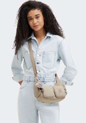 Beige shoulder bag made of soft fabric, featuring two front pockets, a subtle quilted pattern, and a decorative pom-pom charm.