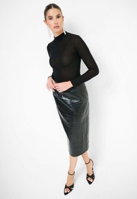 Top lungo a maniche trasparenti nere abbinato a una gonna midi in pelle nera aderente. L'outfit presenta una texture liscia e una leggera lucentezza. Tacchi aperti neri.