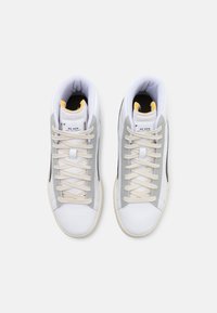 Vysoké tenisky s bílou kůží, šedými semišovými akcenty a krémovými šňůrkami. Polstrovaný límec, gumová podešev a černý boční detail.