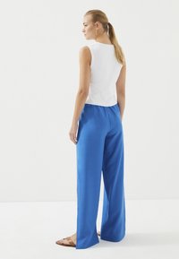 Witte geribde tanktop gecombineerd met luchtige felblauwe wijde broek. Glad materiaal met zijsplitten, aangevuld met platte sandalen.