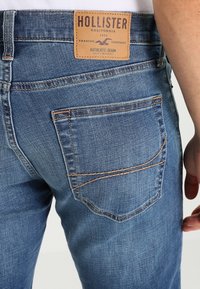 Blå denimjeans med avslappnad passform, med en läderlogotyp, subtil sömnad på fickorna och en slät yta.