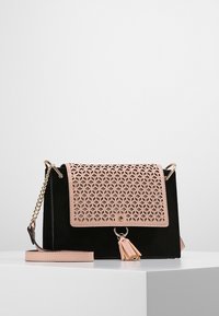 Borsa nera e rosa con un design geometrico ritagliato sulla patta, dettagli in metallo color oro e un accentuato nappina. Texture liscia con una forma strutturata.