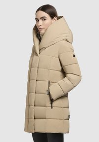 Beige dunjakke med høj krave, quiltet gittermønster, sidelommer og lynlås. Glat tekstur og mellemlang design.