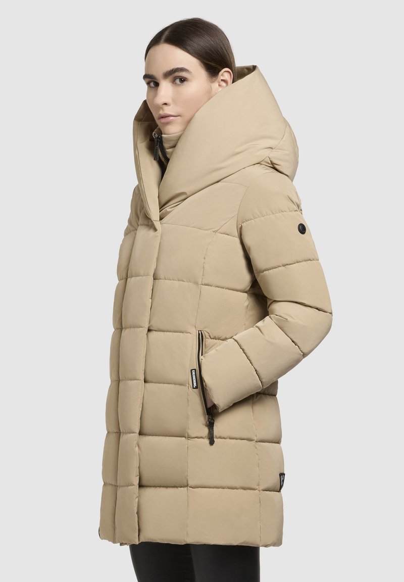 Beige Daunenjacke mit hohem Kragen, genähtem Rautenmuster, seitlichen Taschen und Reißverschluss. Glatte Textur und mittellanges Design.