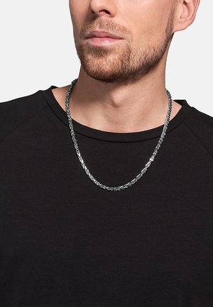 Silberne Kettenhalskette mit strukturierten Gliedern, getragen über einem schwarzen Shirt, mit flachem Design und wechselnden Mustern im Metall.