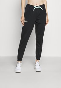 Pantalones deportivos negros de material suave con un cordón verde menta, bolsillos laterales, puños elásticos y una pequeña etiqueta en la parte delantera.