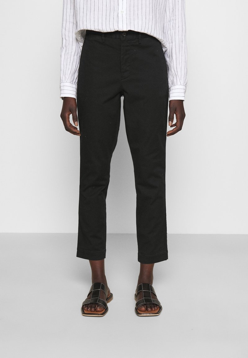 Pantalon noir en coton à coupe droite, avec fermeture à bouton et revers roulés, assorti à des sandales marron à bout ouvert.