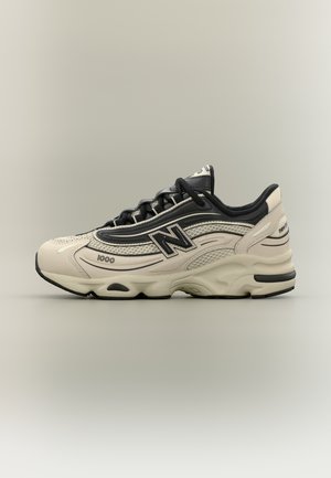 Μπεζ και μαύρο αθλητικό παπούτσι New Balance 1000 με επάνω μέρος από δίχτυ και δέρμα, χοντρή σόλα και μαύρα κορδόνια, εμφανιζόμενο σε προφίλ σε ουδέτερο φόντο.