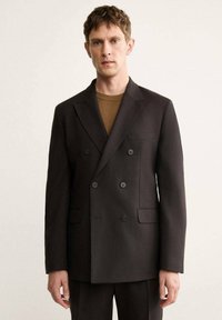 Blazer doppiopetto marrone scuro, realizzato in tessuto texture, con due tasche frontali, revers a ala di rondine e dettagli con bottoni.