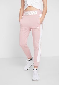 Rosa fleece-joggers med vita sidostripes, elastisk midja med "PUMA"-logotyp och sidofickor. Åtföljd av vita träningsskor.