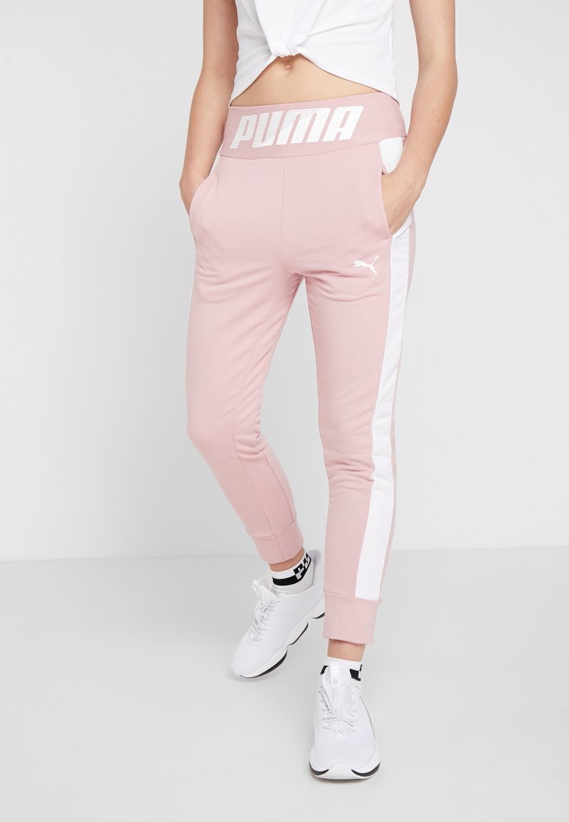 Rosa fleece-joggers med vita sidostripes, elastisk midja med "PUMA"-logotyp och sidofickor. Åtföljd av vita träningsskor.