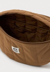 Καφέ υφασμάτινη τσάντα μέσης με ανοιχτό φερμουάρ, αποκαλύπτοντας εσωτερικό με επένδυση και μία μικρή τσέπη μέσα, με ραμμένο λευκό λογότυπο.